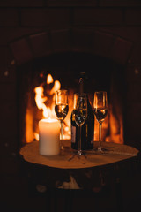 Champagne glasses full of bubbly champagne on the wooden slab table by the burning flames of a fireplace