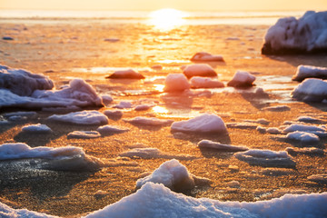 Early winter frosty morning at sea. Snow on the shore, the frozen sea of pink color lit by the sun.
