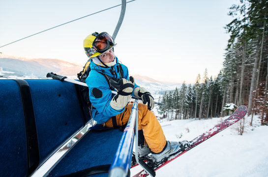 Close-up of skier man sitting at ski chair lift in the evening and looking at the camera with smile