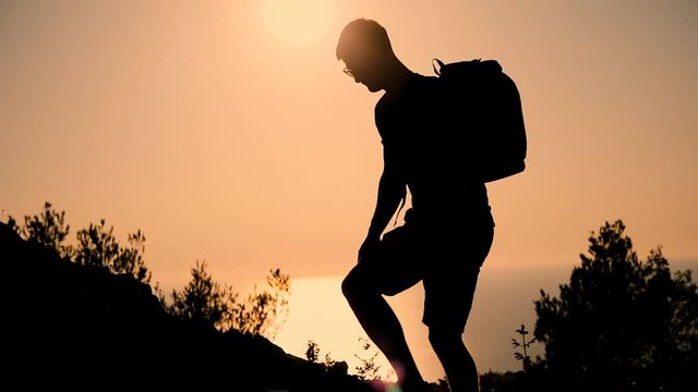 A man with a backpack rises to the top of the mountain at sunset. Silhouette of the person at sunset. Healthy Active Lifestyle.