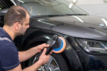 Fototapeta na wymiar A man polishes a black car with a polisher