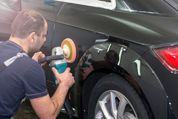 A man polishes a black car with a polisher