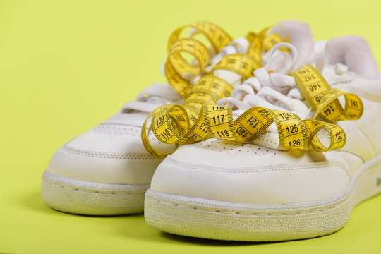 Centimeter in yellow color curled on white trainers, close up.