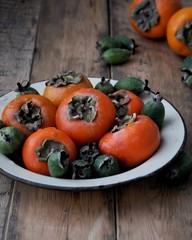 On the table, a fresh persimmon and feijoa on a platter