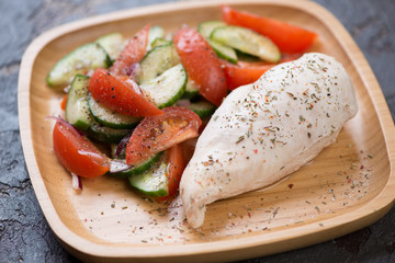 Boiled chicken breast fillet with vegetable salad served on a bamboo tray, studio shot