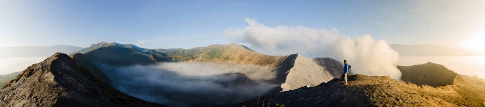 Panorama of Gunung Bromo inner volcano crater, with sulphur fumes and morning mist at sunrise, in Java, Indonesia, with one male adult gazing.