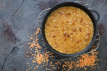 Thick indian red lentil soup masoor dahl in a cast-iron pan. View from above on a cracked asphalt background with copyspace