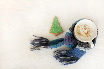 warming Christmas coffee break/ mug with frothy cappuccino wrapped in a blue scarf next to a ginger fir tree top view