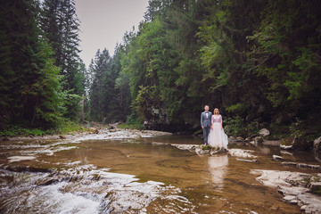 Groom in grey suit and bride in a light dress pose on the rocks before a mountain river