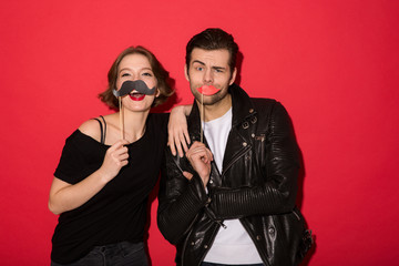 Funny cheerful punk couple posing with fake mustache and lips