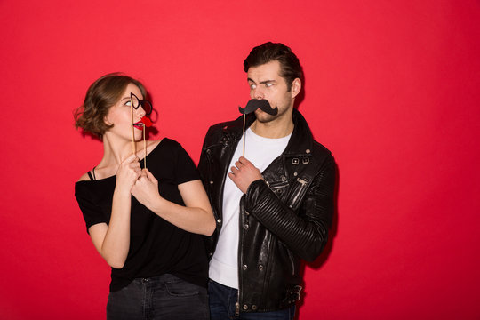 Playful punk couple posing with fake mustache, lips and eyeglasses