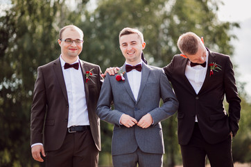 Handsome groom and groomsmen pose outside before large old trees
