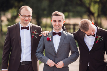 Handsome groom and groomsmen pose outside before large old trees