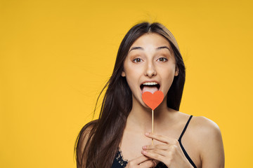 1990672 Beautiful young woman on a yellow background holds paper accessories for parties