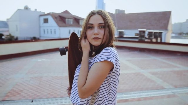 Close-up of a pretty hipster girl posing with a skateboard at the city street