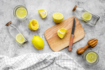 Prepare refreshing beverage lemonade. Lemons, juicer, bottle, knife, cutting board on grey stone background top view