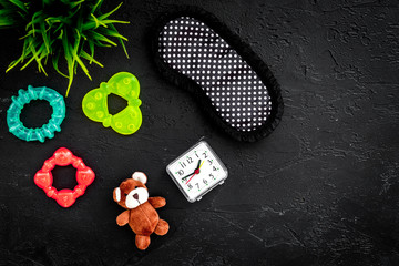 Rest for young mother concept. Sleep mask, plant, alarm clock, toys on black background top view copyspace