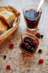 Berries in a basket, roll and tea on the table. Breakfast.