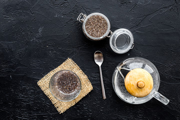 Obraz na płótnie Canvas Brew chia seeds. Jar with seeds, scoop, bowl, tea pot with hot water. Black background top view copyspace