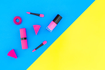 Bright decorative cosmetics. Pink nail polish and lipstick on blue and yellow background top view copyspace