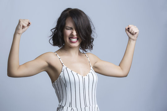 Ragazza vestita con abito bianco a righe nere con bretelline , ci mostra i muscoli sforzando - sfondo chiaro