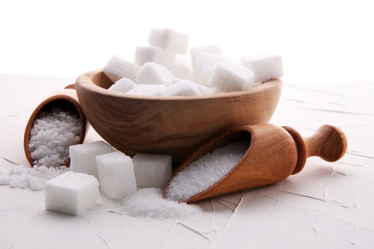 Close up the sugar cubes and cane in wooden spoon on the table.