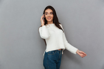 Young pretty woman in white sweater and jeans speaking on mobile phone, looking aside