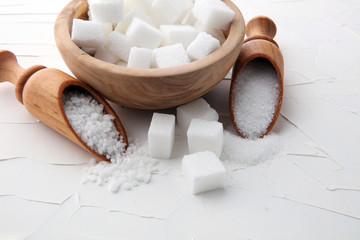 Close up the sugar cubes and cane in wooden spoon on the table.