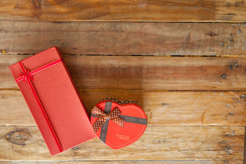 Red gift box and red ribbon and mini heart inside on wood background with space..