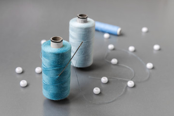 Reel of blue threads with a needle on a gray background