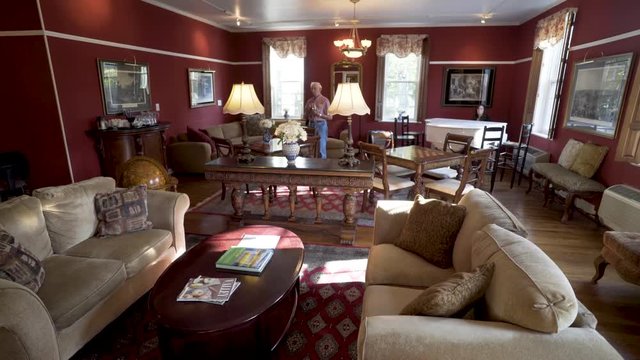 An elderly man stands and looks around in a large lounge filled with couches and seating and a grand piano.