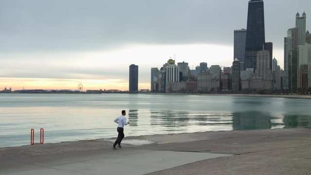 Man is running on thr ebankment. Athlete training outdoors. Sea, Downtown with skyscrapers on the background. Morning sunrise.