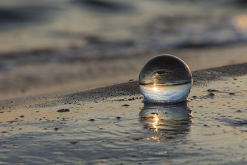 Arte attraverso la sfera di cristallo,sfera adagiata sulla spiaggia e bagnata dal mare.