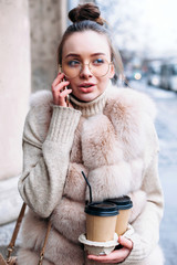 Young fashion pretty sensual woman outdoor street cold winter weather portrait. A girl walking the street and speaking mobile phone.