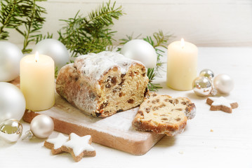 criststollen, typical german christmas cake with candles, baubles and cinnamon star cookies on a rustic white wooden table