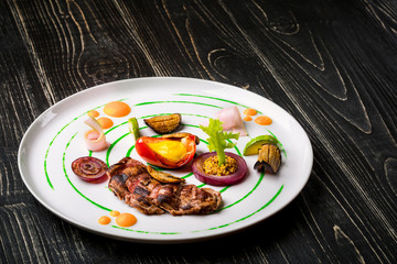 Sliced meat with fresh herbs, vegetables and spices on a white plate on a black wooden background, top view