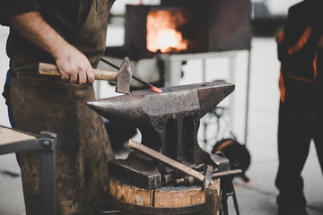 The blacksmith manually forging the molten metal on the anvil in smithy with spark fireworks (color...