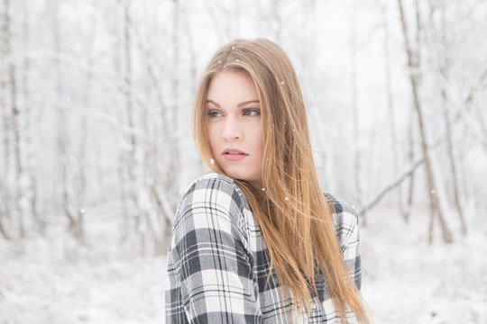 Young woman in black and white plaid shirt stading in a snow covered forrest.