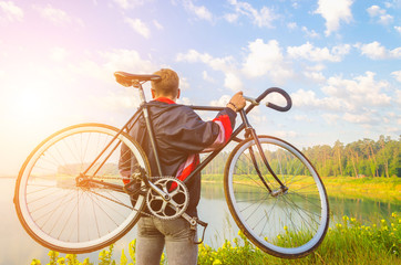 Fototapeta premium man stand with bicycle in hands on the hill and looking at the lake with azure water. sunrise
