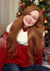 Beautiful redhead girl portrait in christmas decoration. Home interior with fir tree and gifts. New year eve and winter holiday concept.