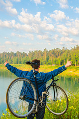 man stand with bicycle in hands on the hill and looking at the lake with azure water. sunrise
