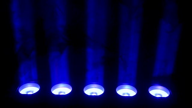 Blue spotlight and smoke on black background. Abstract dark background with bright blue stage spotlights. Lights and smoke. Row of blue lights from a stage.