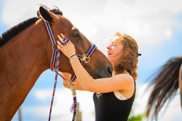 Jockey young girl petting and hugging brown horse