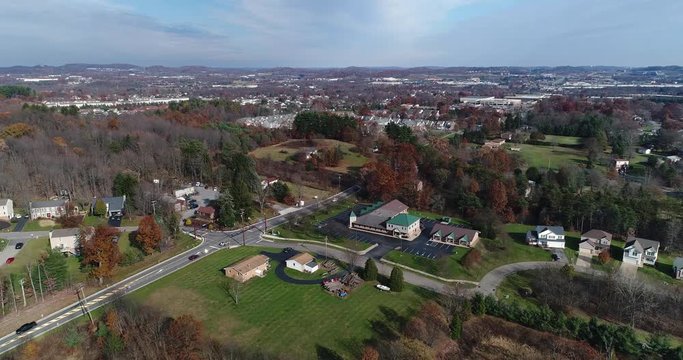 A daytime slow forward aerial establishing shot of a typical Western Pennsylvania small town or village intersection. Pittsburgh suburbs.  	