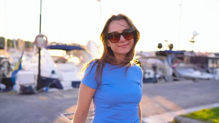 Woman in sunglasses walking along the dock with a lot of yachts and boats at sunset, close up