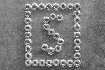 The letter s of the English or Latin alphabet lined with metal nuts. Around the letter's frame of shiny new nuts. The nut and the letter s lying on a metal chrome-plated Board.