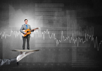 Businessman on metal tray playing acoustic guitar against concrete wall background with charts