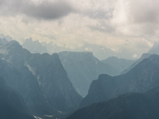 Zoom on mountain peaks and a distnat valley covered in clouds in the Italien alps, Southtirol