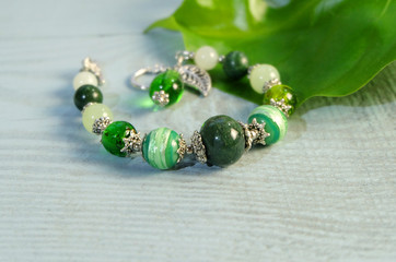 Bracelet of Murano glass and stones in green on a wooden table with a green leaf.