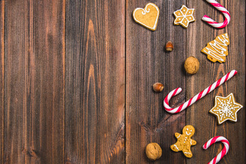 Christmas candy canes, gingerbreads of different shapes, hazelnuts, walnuts on a brown wooden table. Copy space.